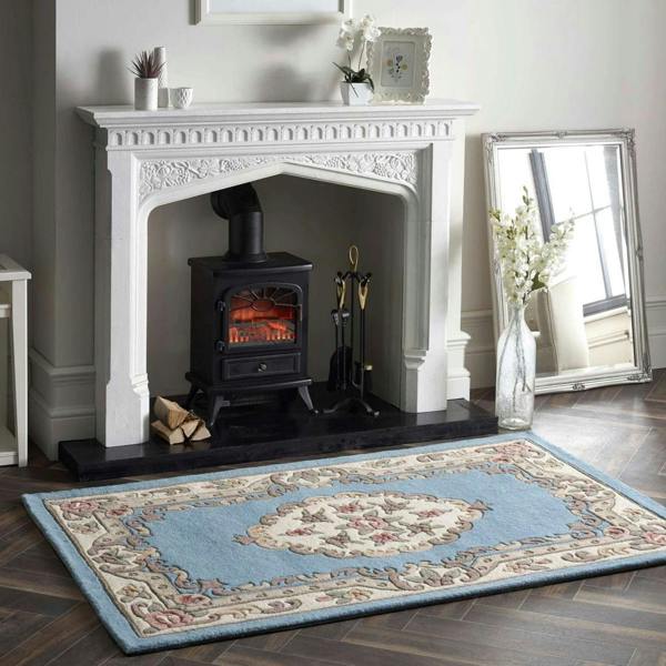 White fireplace with a black stove, decorative items, and a patterned rug on a wooden floor.