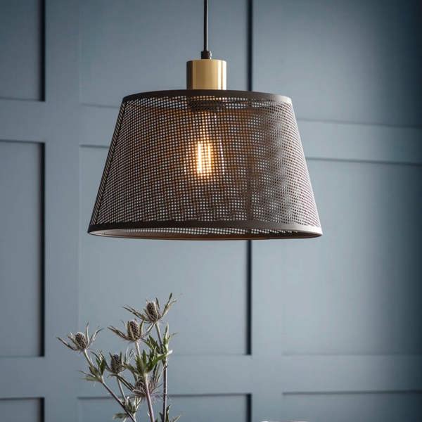 A single black steel mesh pendant light with a brushed brass fitting illuminated against a textured grey background by Abode Home & Gifts.