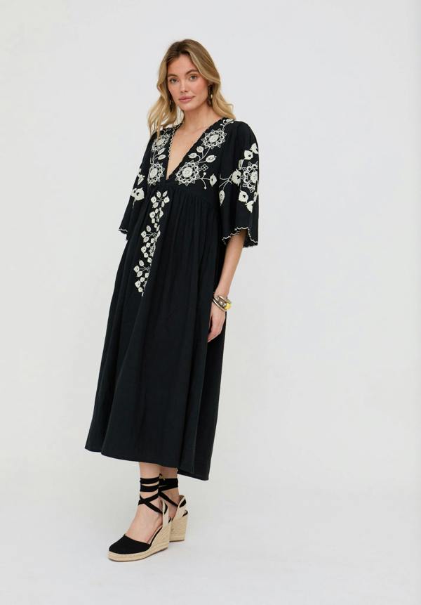 Woman wearing a black dress with white floral embroidery on a white background