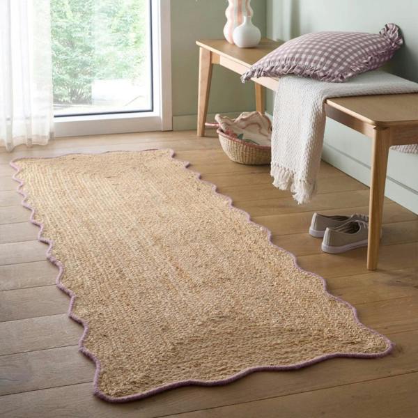 Beige woven rug on a wooden floor with a bench and window in the background