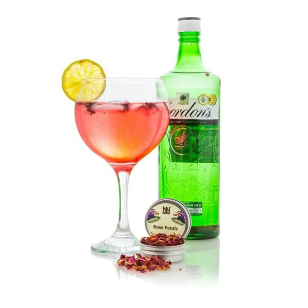 A Glass of Gin Infused with Natural & Noble Rose Petals next to a Bottle of Gin