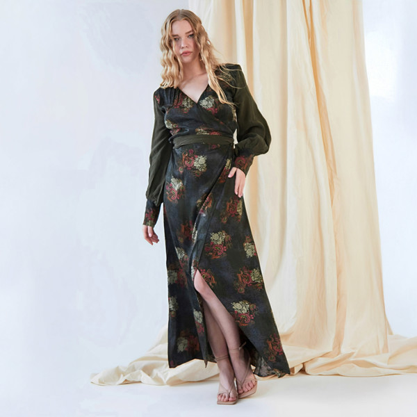 A woman in a Sarvin long sleeve wrap dress standing in front of a curtain.