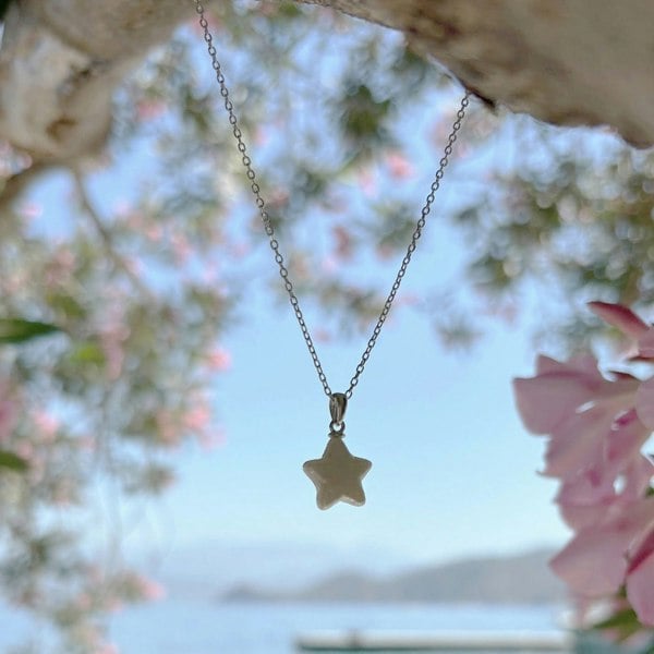 Shimmering pearl star pendant necklace on a silver chain, captured outdoors with a beautiful view.