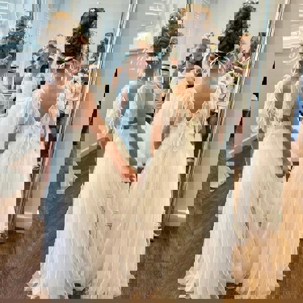 Two young girls in white dresses standing in front of a mirror.