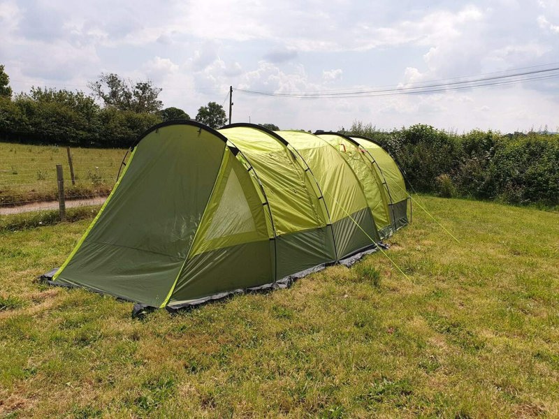 An image of the Abberley XL Extension by Olpro attached to the Abberley XL Tunnel Tent on a camping field with the front closed and window blind closed.