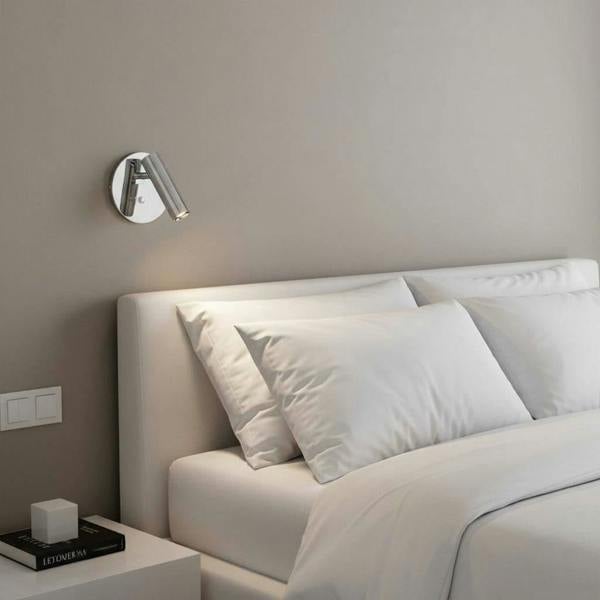 Polished chrome recessed bed reading lamp mounted next to a bed on the wall in a modern bedroom 