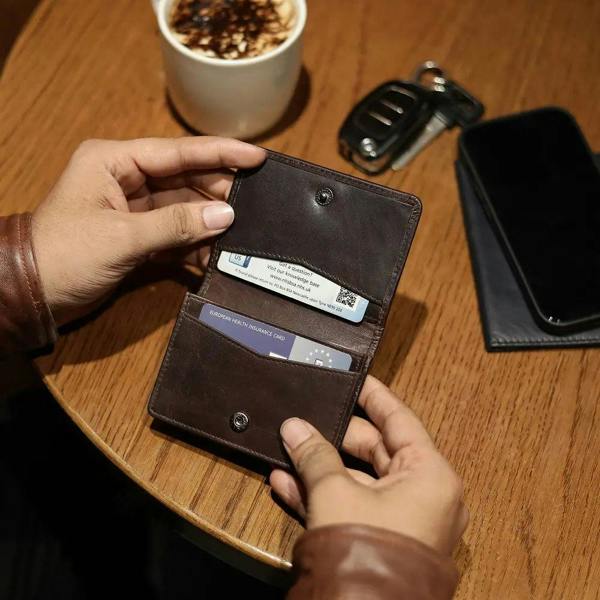 Brown leather Mayfair 2511 credit cardholder being used on a wooden café table beside a coffee cup and phone.