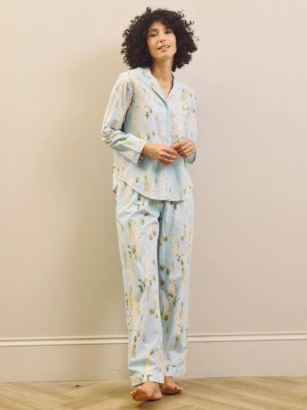 Woman wearing a light blue floral pyjama set against a beige wall.