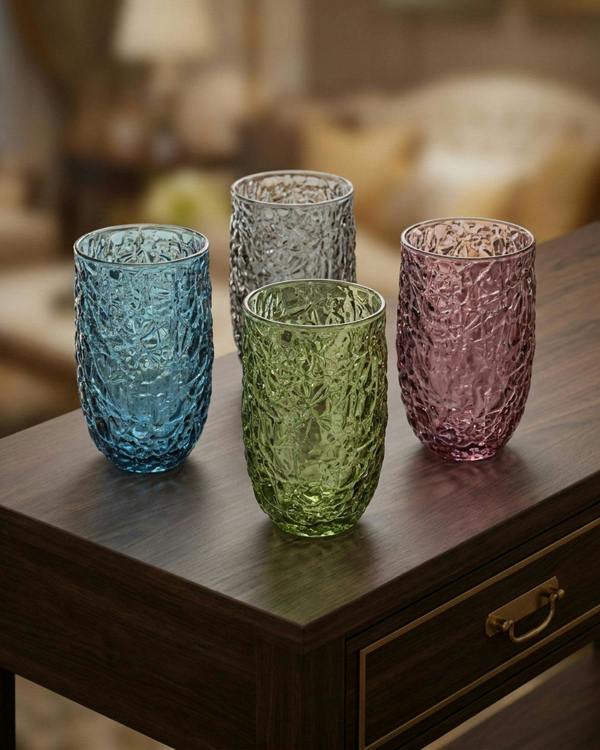 Four textured glass tumblers in blue, green, and pink on a wooden table with a blurred background.