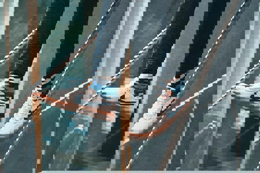 Person wearing white sneakers with striped socks, standing on a metal railing.