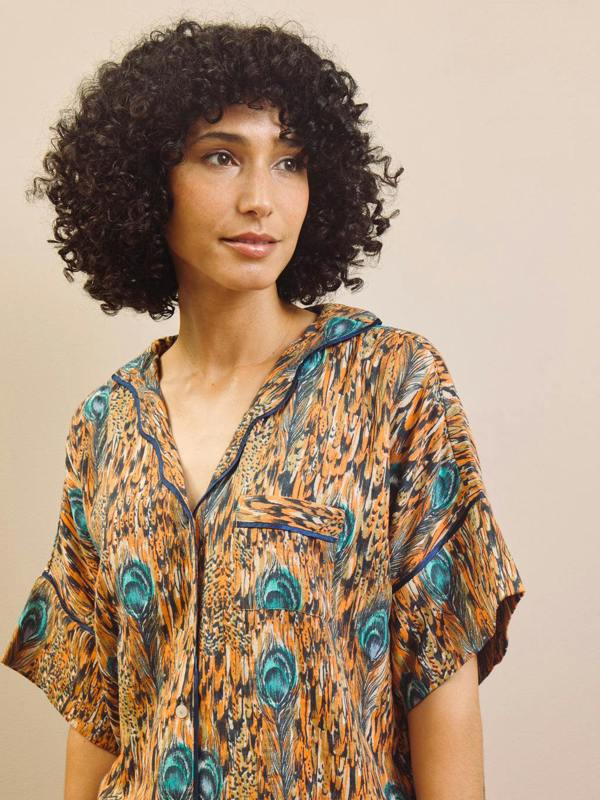 Woman wearing a patterned  pyjama shirt with peacock feathers on a beige background