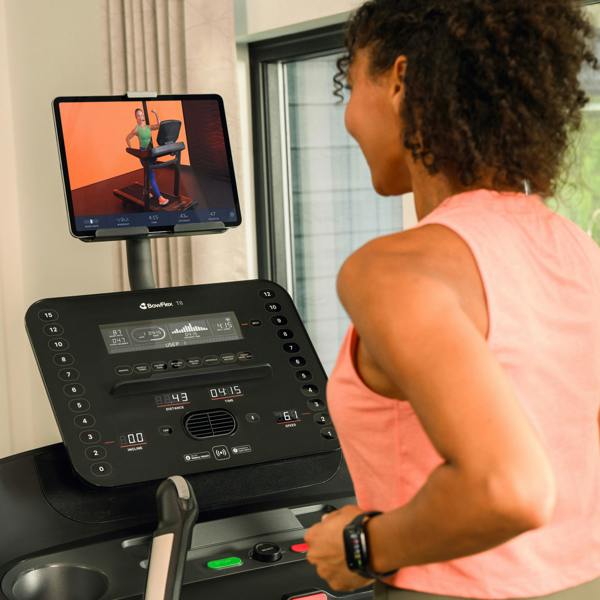 Woman using a treadmill with a tablet displaying a workout video on the screen.