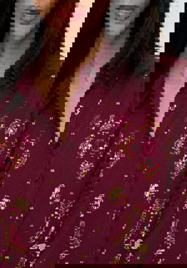 Close-up of a person wearing a maroon shirt with intricate gold and pink patterns.