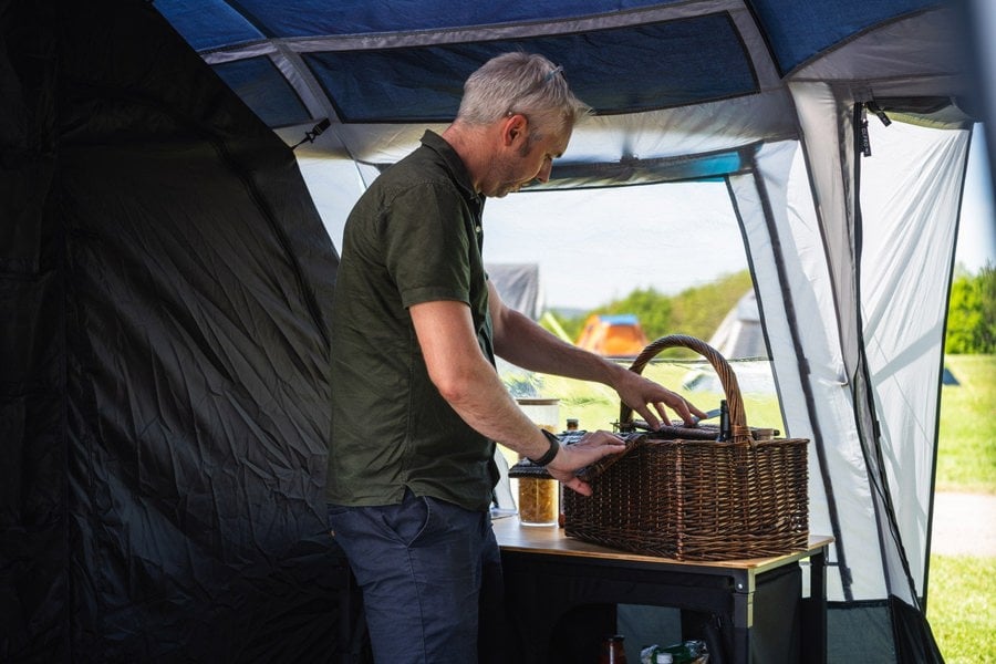 A man prepares a drink on an OLPRO Camp Kitchen inside the Stafford 8.0 Poled Family tent