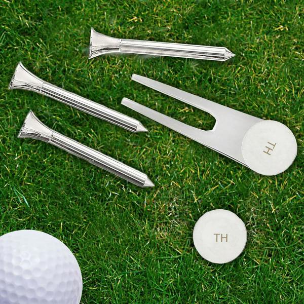 Silver-plated personalised golf green set featuring three tees, a pitch repairer, and ball markers engraved with initials, displayed on grass with a golf ball.