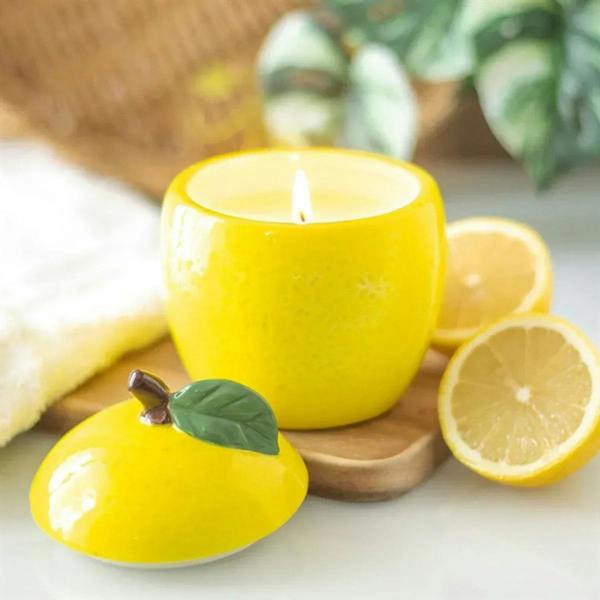 Yellow lemon-shaped candle jar with open top and burning wick, glossy ceramic.
