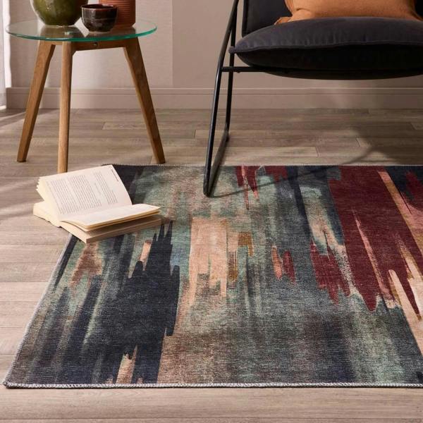 Colorful abstract rug on a wooden floor with a chair and small table in the background.