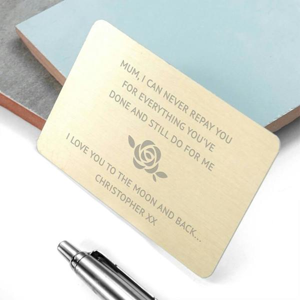 A gold-finished personalised metal wallet keepsake card for Mum engraved with a central rose motif and a heartfelt message on a light desk.