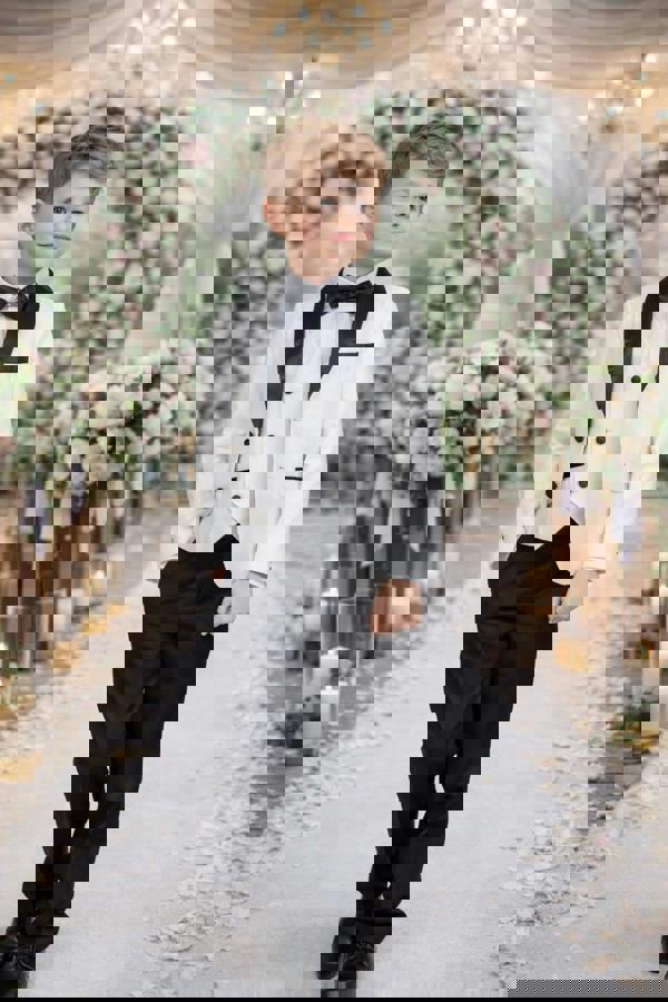 Young boy in a formal outfit walking down a decorated wedding aisle with flowers and candles.