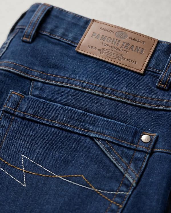 Close-up of blue jeans with a Pamoni Jeans label on a light gray background