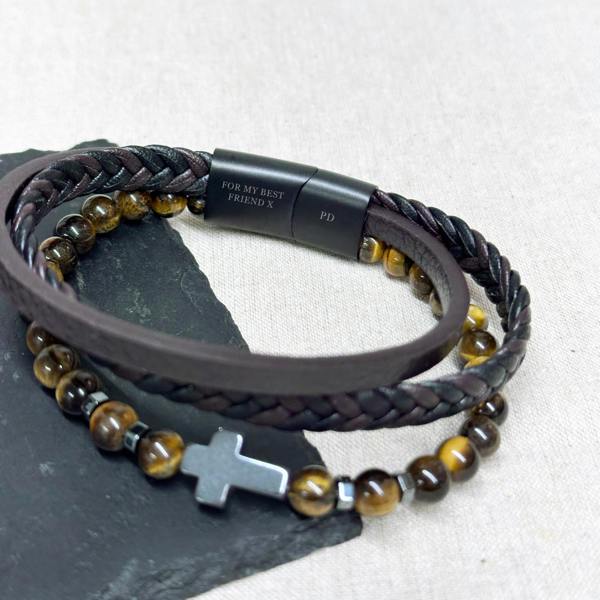 A men's layered bracelet featuring brown leather strands, Tiger's Eye beads, a steel cross, and a black clasp engraved with 'For my best friend'.