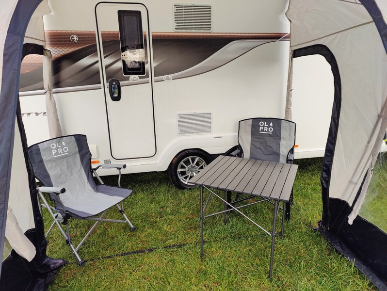 An image of the View Lite 260 Caravan Awning from OLPRO in a field attached to a caravan with some camping furniture inside.