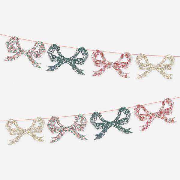 Eight 3D paper bow pennants featuring assorted festive Liberty floral prints, displayed in two parallel rows against a plain white background.