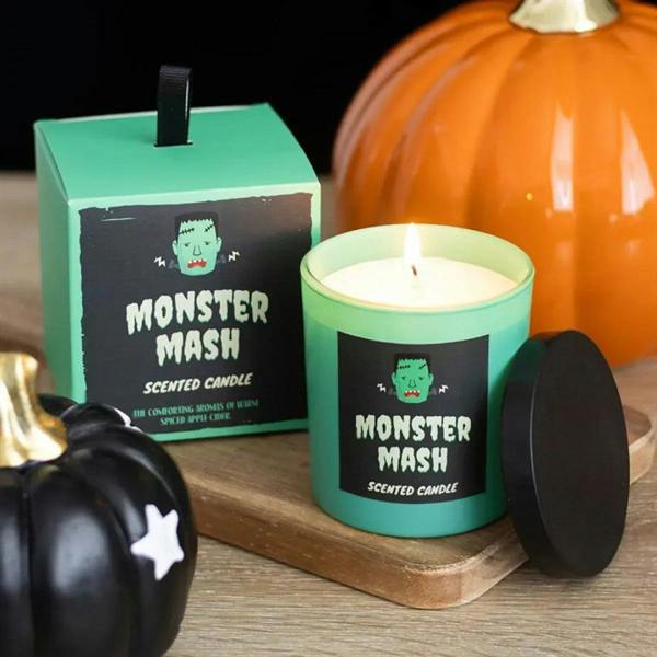 Teal scented candle in jar with lit wick, black label and green monster graphic, lid