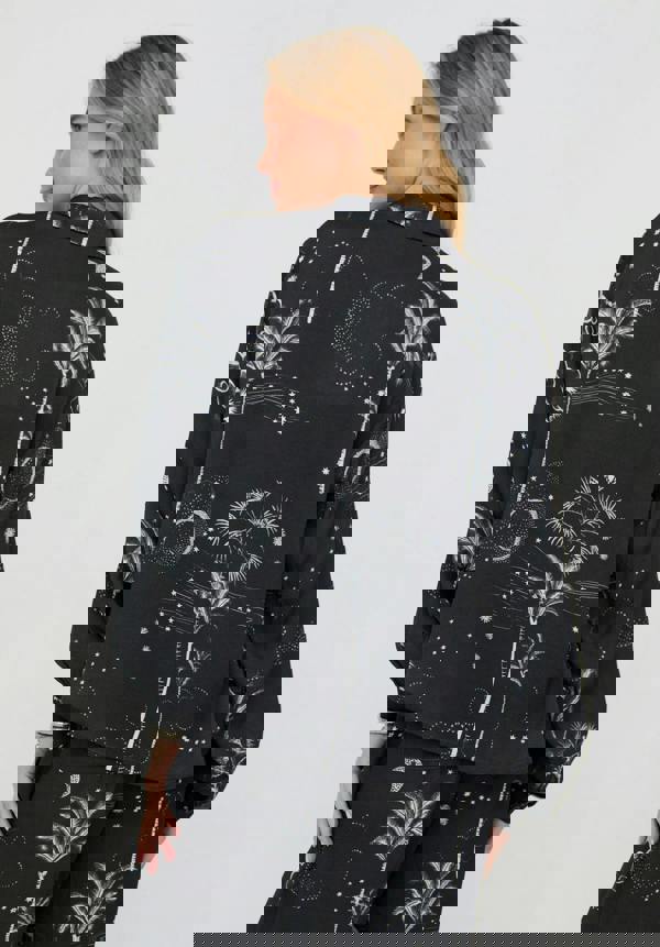 Woman wearing a black outfit with white floral and moon pattern on a plain background