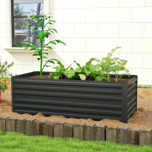 Black outdoor raised bed planter with leafy greens, placed on a stone-edged border