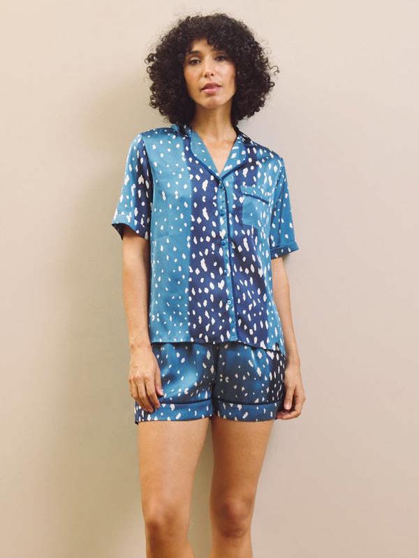 Woman wearing a blue patterned pajama set against a beige wall.
