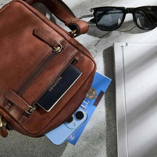 Brown leather bag with sunglasses and phone on a gray surface