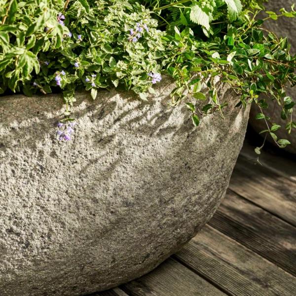 Close-up detail of the textured Cranford planter rim showing the robust ficonstone material with trailing green foliage and small purple flowers.