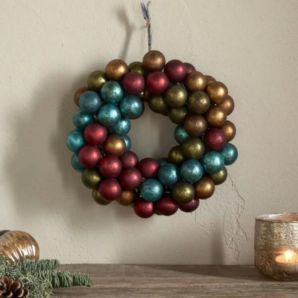 Recycled glass bauble wreath hung on a wall above a rustic wooden shelf with a flickering candle.