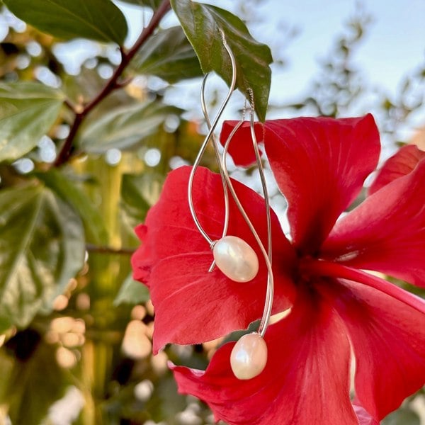 Shimmering pearl threader earrings swaying against a red hibiscus.