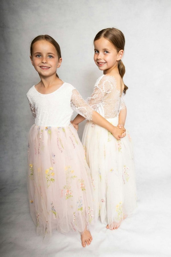 Two young girls in matching floral dresses standing against a neutral background