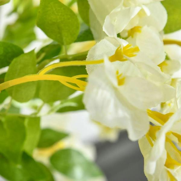 Close-up of white faux wisteria blossoms with green leaves on artificial stems