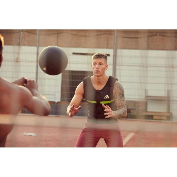 Man playing with a medicine ball on an outdoor court, wearing an adidas weighted vest.