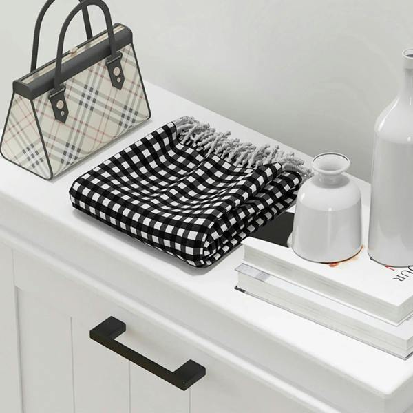 White cabinet top with a folded plaid blanket and a black-handled bag next to vases