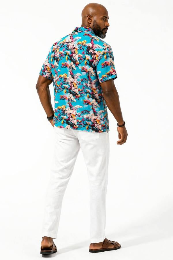 Man wearing a colorful floral shirt and white pants on a white background