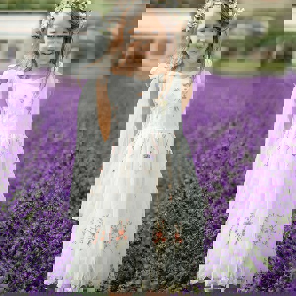 Young girl in a white dress with floral patterns standing in a lavender field.