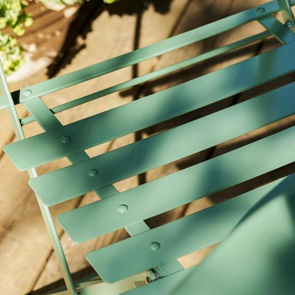 Close-up top-down view showing the smooth slatted metal seat and rivets of a thistle green folding bistro chair on a wooden deck.