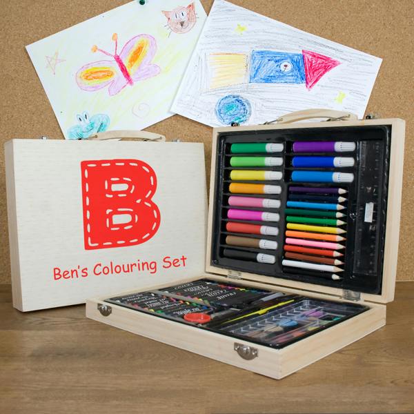 A 63-piece personalised children's colouring set in a wooden case printed with a large red letter B and Ben's Colouring Set, open on a desk displaying art supplies alongside drawing artwork.