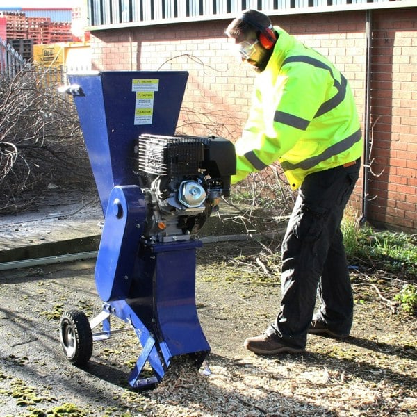 T-Mech 15HP wood chipper in blue with a large funnel, man in safety gear operating it on a path covered in wood chips