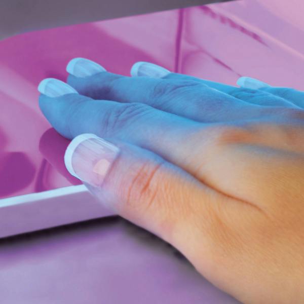 ladies hand under UV nail lamp curing gel nail extensions