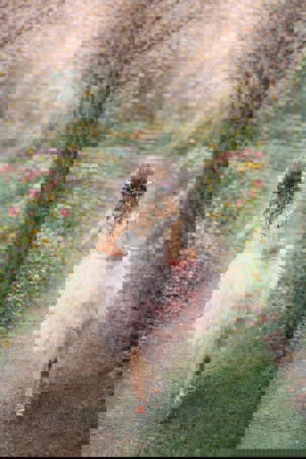 Young girl in a pink dress walking through a garden with cherry blossom trees.