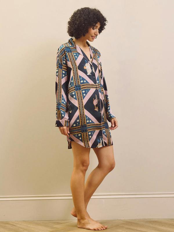 Woman wearing a patterned nightshirt dress against a plain wall