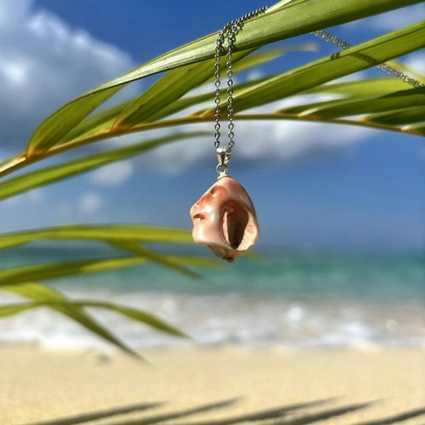 Salmon shell pendant charm by LENAE, handcrafted in London and displayed on an exotic Cayman Islands beach.