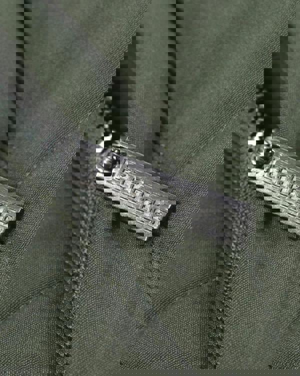 Lambretta Mens Padded Hooded Classic Badge Parka, close-up of the metal zipper pull featuring the 'Lambretta' logo on a dark green fabric jacket.