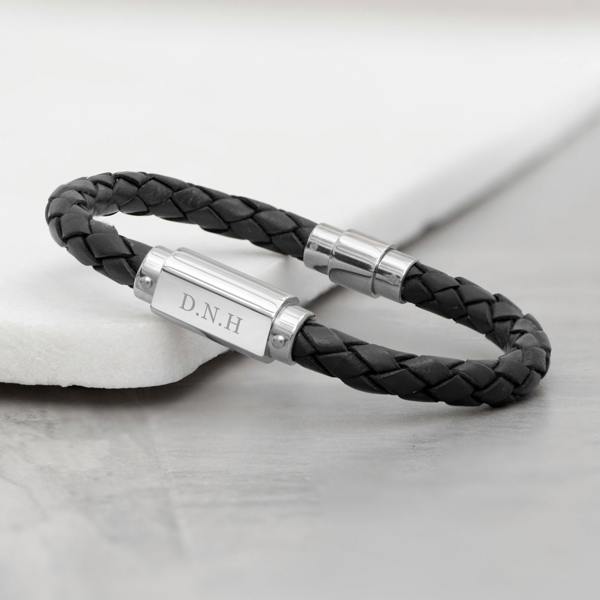 Personalised men's black braided leather bracelet resting on a marble surface with a stainless steel plate engraved with D.N.H